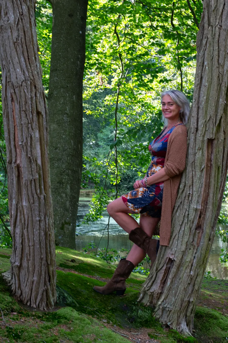 Marleen Postmus, coach en massagetherapeut van praktijk Innerlijk Geluk, staand tussen twee bomen aan de waterkant in een bos.